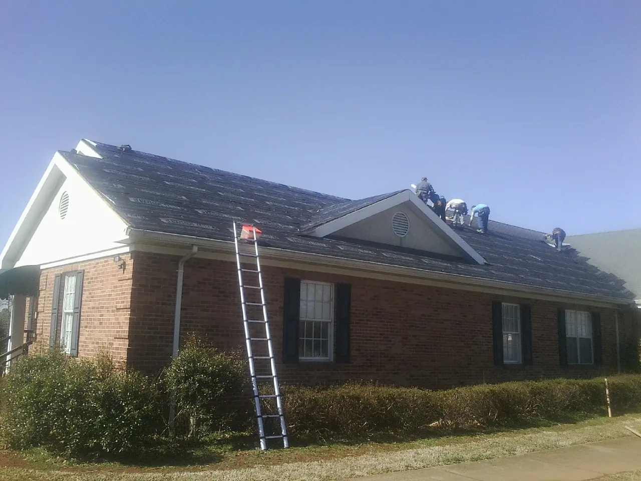 Crew tearing shingles off a brick ranch roof with a ladder set — Metal Roof Repair work by our crew in Mccordsville