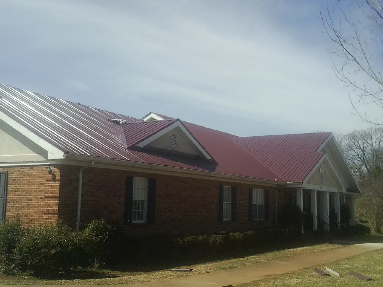 Red metal roof with gabled entries on a long brick building, from a Hail Damage Roof Repair job in Mccordsville
