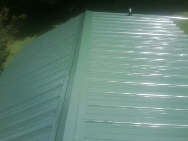 New green metal panels meeting at the ridge of a roof — Flat Roof Repair work by our crew in Mccordsville