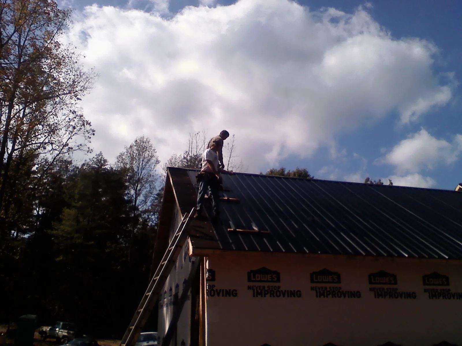 Roofer fastening dark metal panels high against a cloudy sky, from a Roof Inspection job in Mccordsville