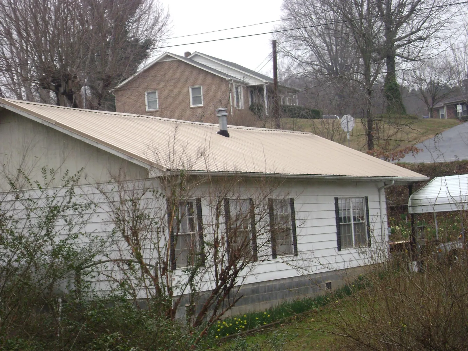 Tan metal roof on a white sided house set into a hillside — Commercial Roofing by Roofing Brothers in Mccordsville
